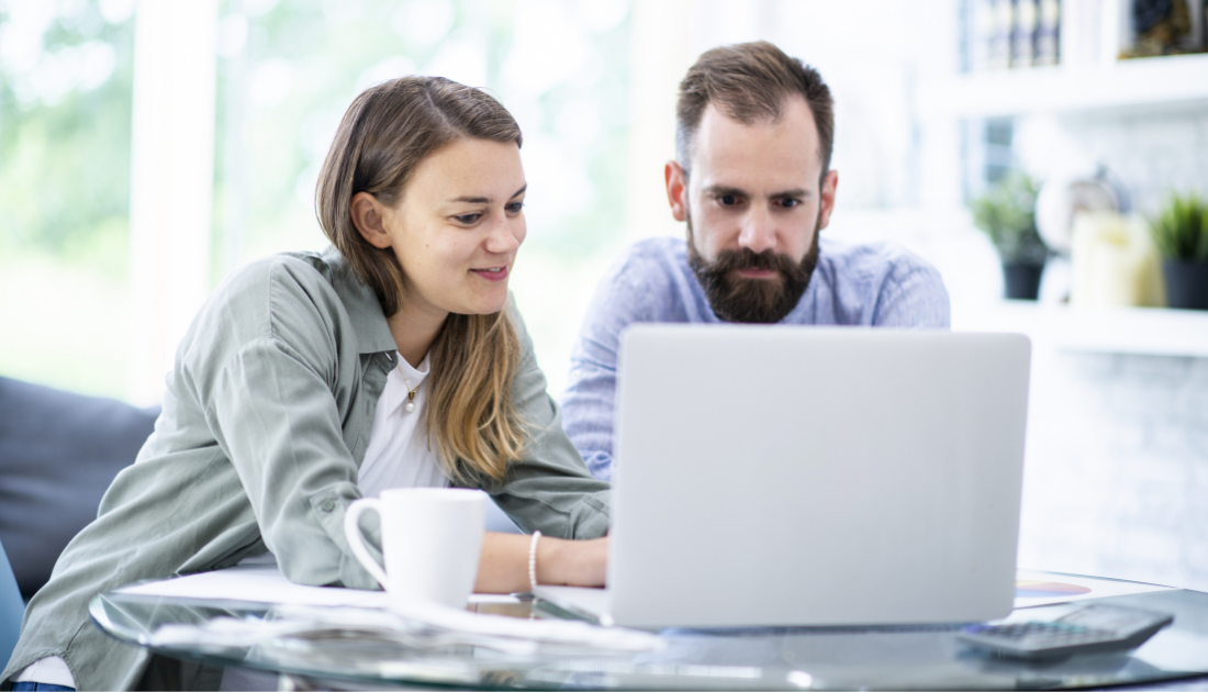 happy young couple reviews health insurance plans on laptop at home